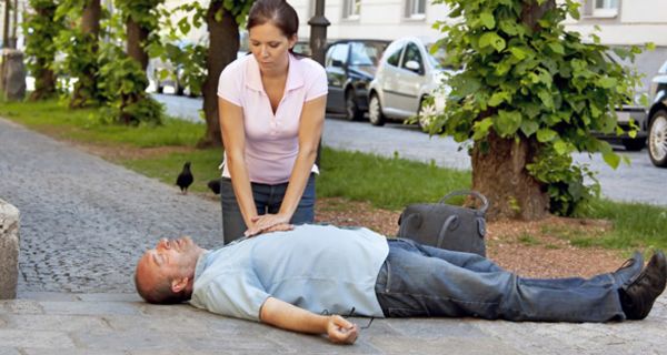Frau wendet bei auf der Straße liegendem Mann Herzdruckmassage an
