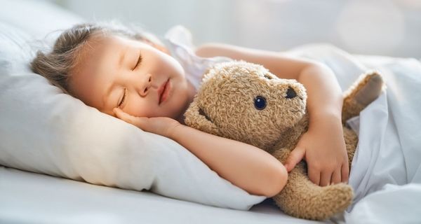 Mädchen schläft mit Teddy im Arm.