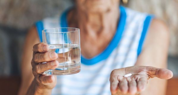 Ältere Frau mit Wasserglas und Tablette.