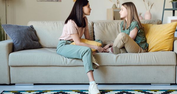 Zwei Mädchen sitzen auf einem Sofa und unterhalten sich.
