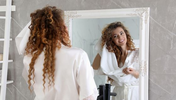 Frau steht mit Handtüchern vor dem Spiegel im Badezimmer