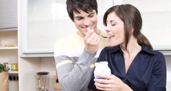 Mann gibt Frau einen Löffel Joghurt.