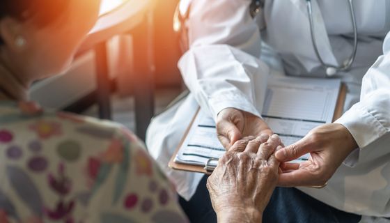Arzt begutachtet die Hand einer älteren Patientin.