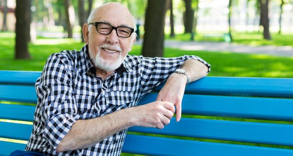 Älterer Mann mit Brille und Bart sitzt auf einer Parkbank.