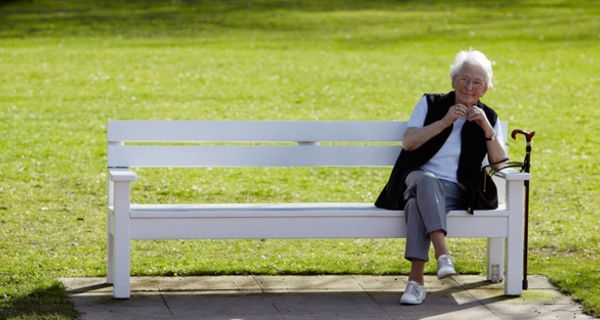 alte Dame sitzt in der Sonne auf einer weißen Parkbank