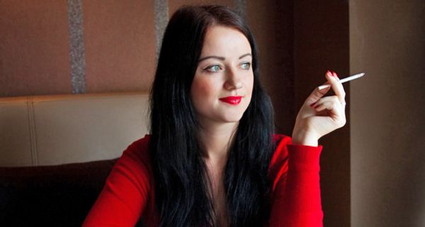 Dunkelhaarige, junge Frau mit einem roten Pullover sitzt in einem Cafe und raucht