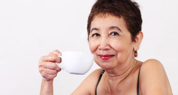 Frau um die 50 mit kurzen dunklen Haaren hält eine Tasse Kaffee in der Hand