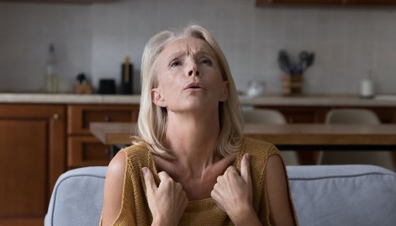 Frau, etwa 50 Jahre alt, zieht ihr Oberteil in der Nähe der Schlüsselbeine vor, um sich zu kühlen.