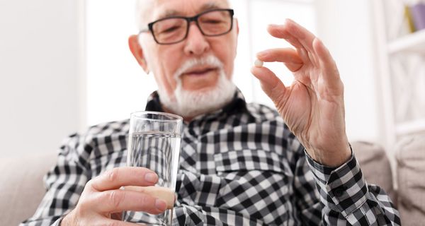 Älterer Mann hält ein Glas Wasser in der Hand und nimmt eine Tablette ein 