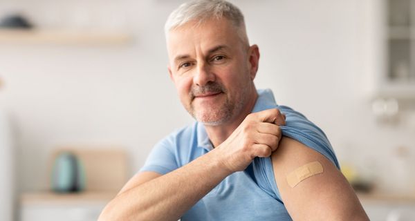 Mann zeigt seinen Oberarm mit Pflaster über der Impfstelle.
