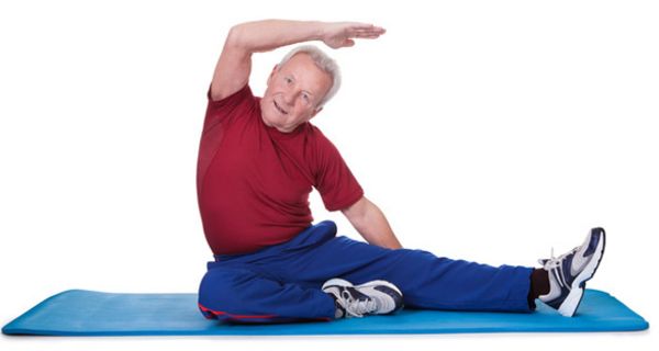 Senior sitzt mit einem seitlich ausgestreckten Bein und einem angewinkelten auf blauer Gymnastikmatte und macht eine Streckübung