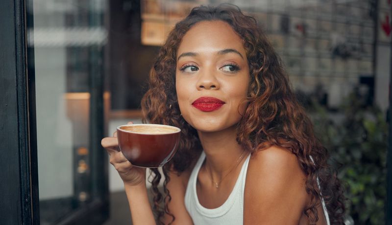 Eine junge Frau trinkt am Fenster Kaffee.