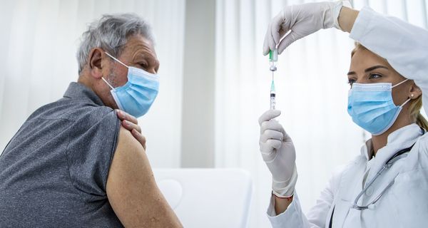 Ärztin, zieht eine Impfspritze auf und bereitet sich darauf vor, Senior zu impfen.