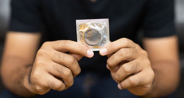 Männerhände halten ein verpacktes Kondom in den Händen.