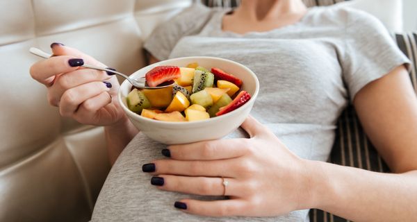 Junge schwangere Frau, isst einen Obstsalat.