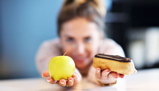 Frau hält Apfel und Schokobrötchen in der Hand.