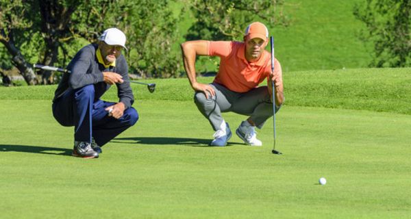 Zwei Golfer hocken auf dem Grün eines Golfplatzes und beurteilen die Situation