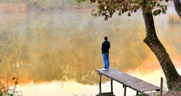 Herbststimmung, Waldsee, Mann steht auf Holzsteg mit Rücken zur Kamera