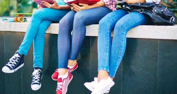 Drei junge, schlanke Frauen sitzen auf einer Mauer, tragen enge Jeans.