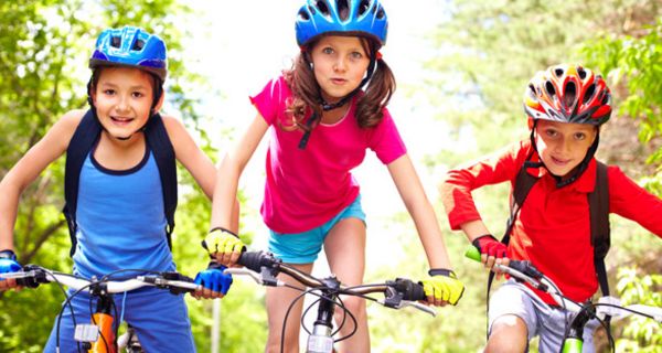 Drei Kinder mit Fahrradhelmen radeln auf einem Weg auf die Kamera zu