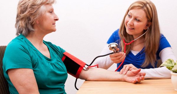 Frau um die 50 bekommt von Pflegerin den Blutdruck gemessen