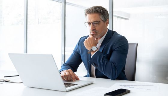 Nachdenklicher Mann in Anzug zwischen 45 und 50 am Laptop im Büro.