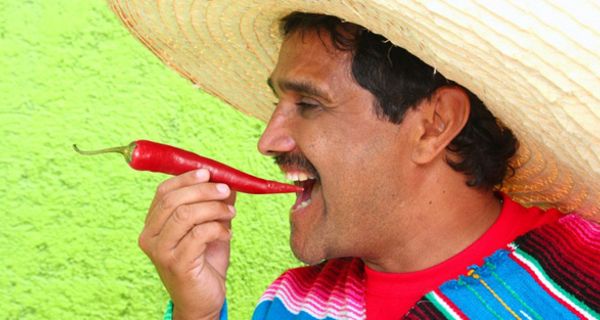 Mexikaner mit Sombrero beißt in Chili-Schote.