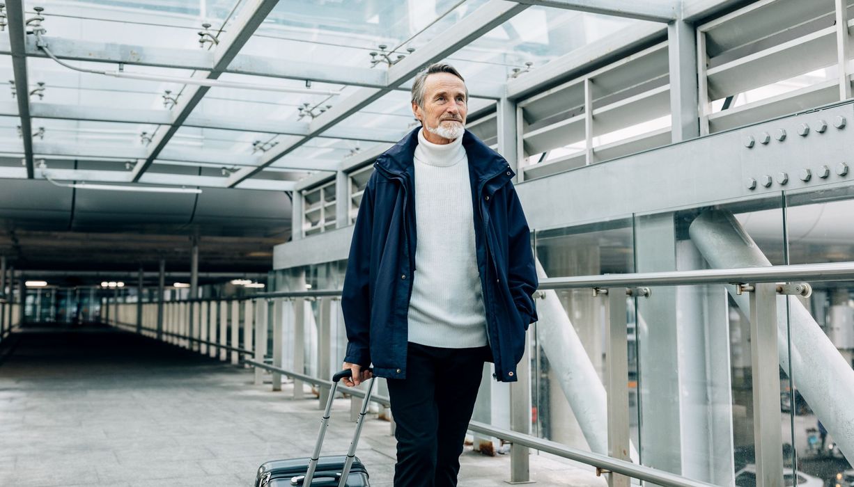 Älterer Mann mit Koffer am Flughafen.