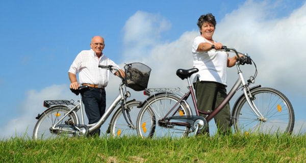 Senioren-Paar, das Fahrräder über eine Wiese schiebt