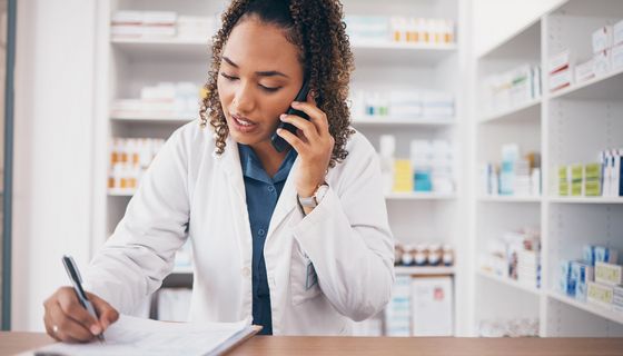 Apothekerin am Telefon, die sich mit einer Hand etwas notiert.