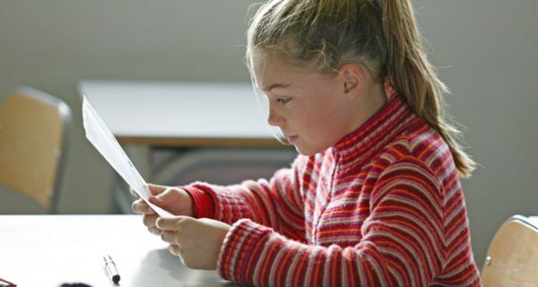Schülerin, ca. 8 Jahre, Profilbild, Pferdeschwanz und rot geringelter Pulli, liest konzentrirt im Klassenraum von einem Blatt