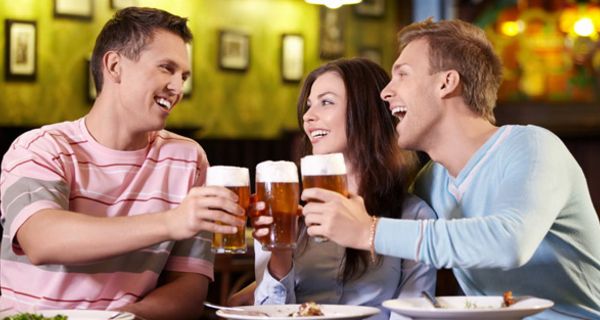 Zwei junge Männer und eine junge Frau stoßen mit Biergläsern an