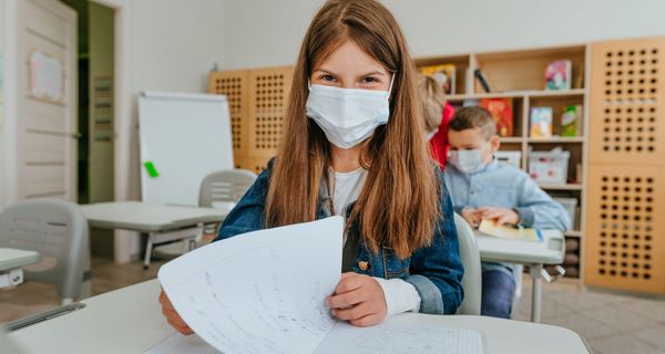 Junges Mädchen mit OP-Maske im Klassenzimmer.