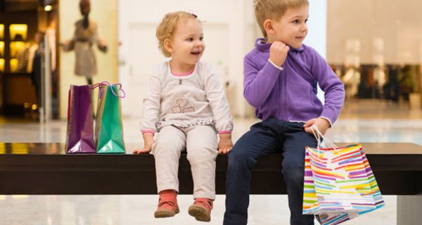 Kleiner Junge und seine kleine Schwester sitzen in einem Einkaufszentrum auf einer Bank