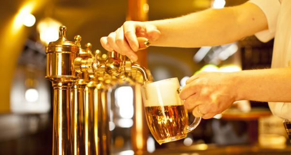 Bierzapfanlage in Kneipe/Pub, Arm von rechts ins Bild ragend zapft gerade ein Bier in einen Humpen.