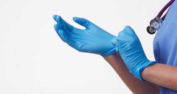 Blaue Einmalhandschuhe (Gummihandschuhe) werden von tw. zu sehender Person im blauen OP-Kittel mit Stethoskop um den Hals angezogen