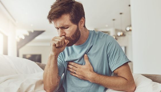 Mann mit Lungenentzündung: Er hält sich die Brust und hustet stark in die geschlossene Faust.