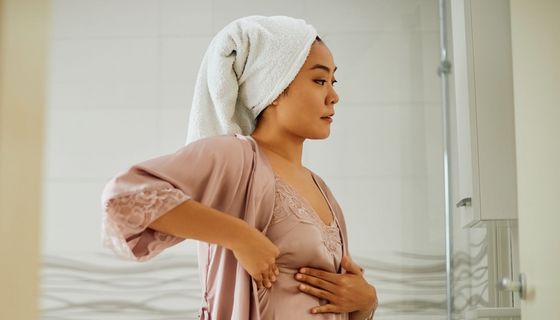 Junge Frau tastet sich im Badezimmer die Brust ab.