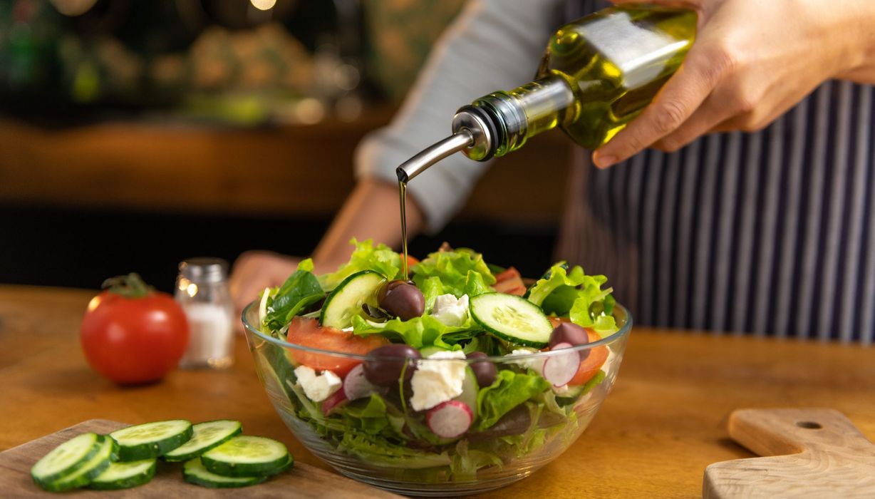 Mann, träufelt Olivenöl auf seinen Salat.