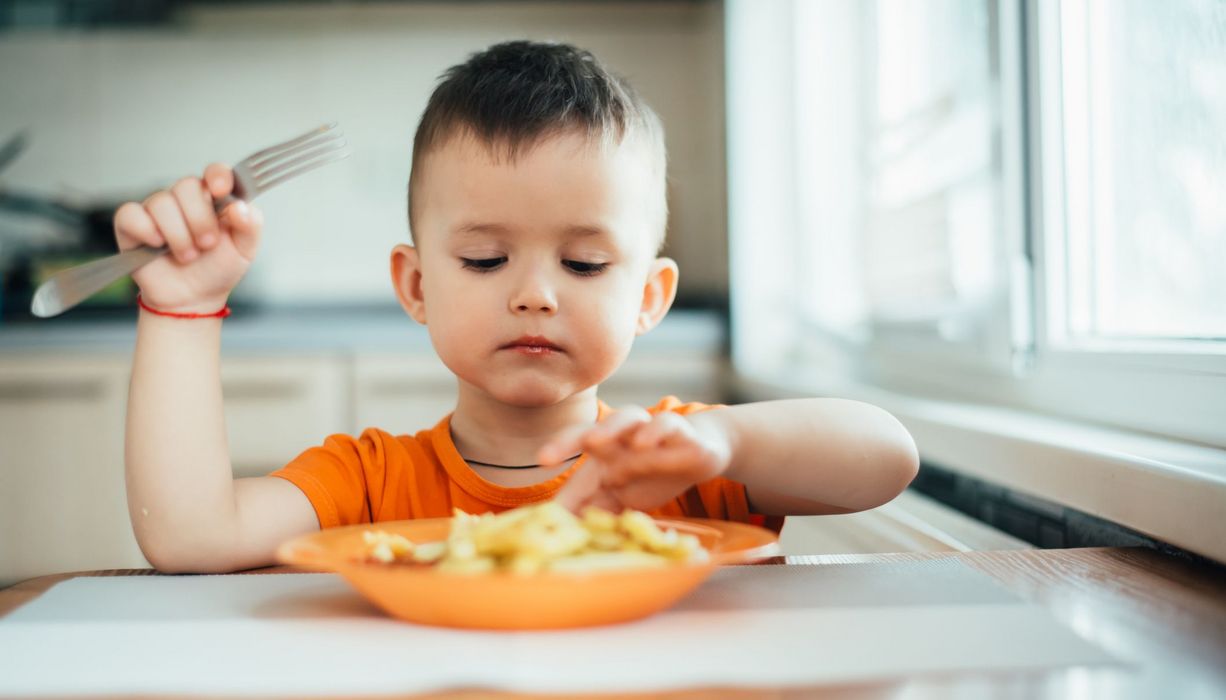 Kleinkind, sitzt an einem Tisch und isst Pommes.