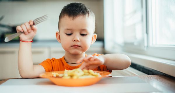 Kleinkind, sitzt an einem Tisch und isst Pommes.