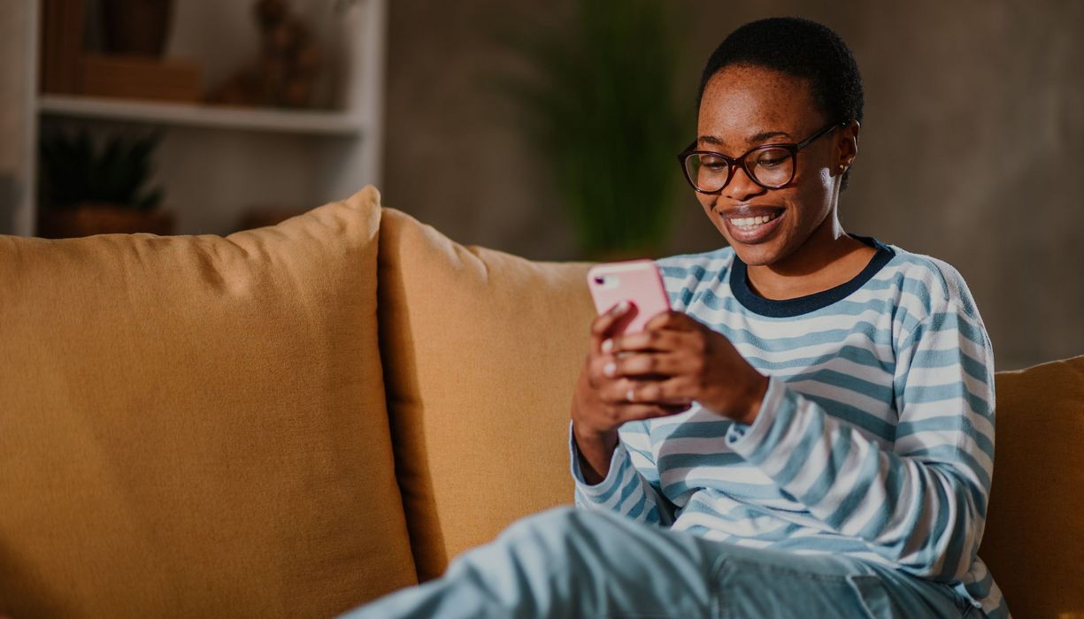 Frau, lächelt und schaut auf ihr Smartphone.