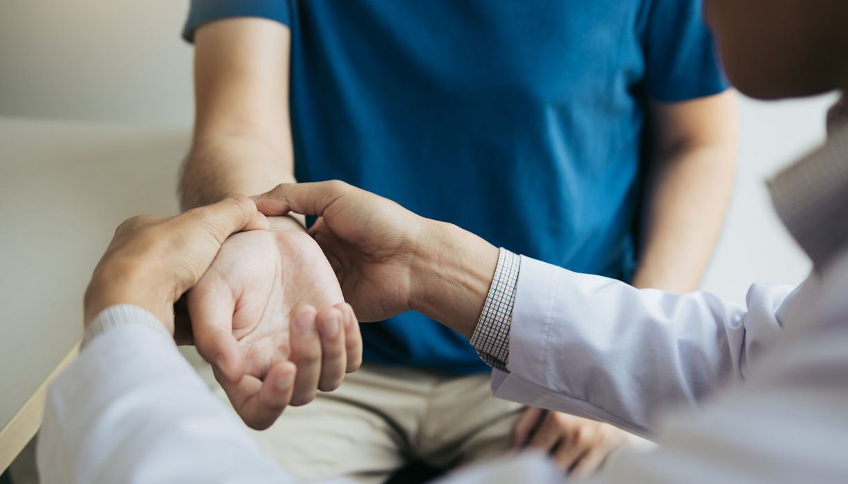 Arzt tastet das Handgelenk eines Patienten.