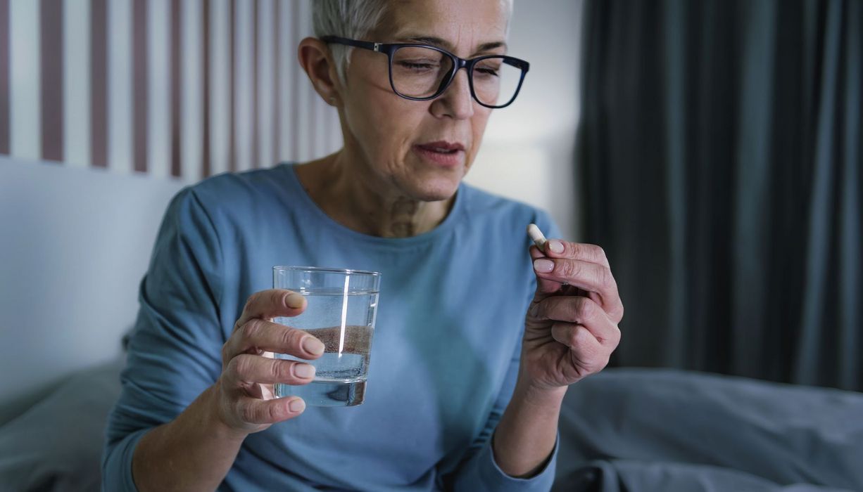 Seniorin nimmt Tablette mit einem Glas Wasser.