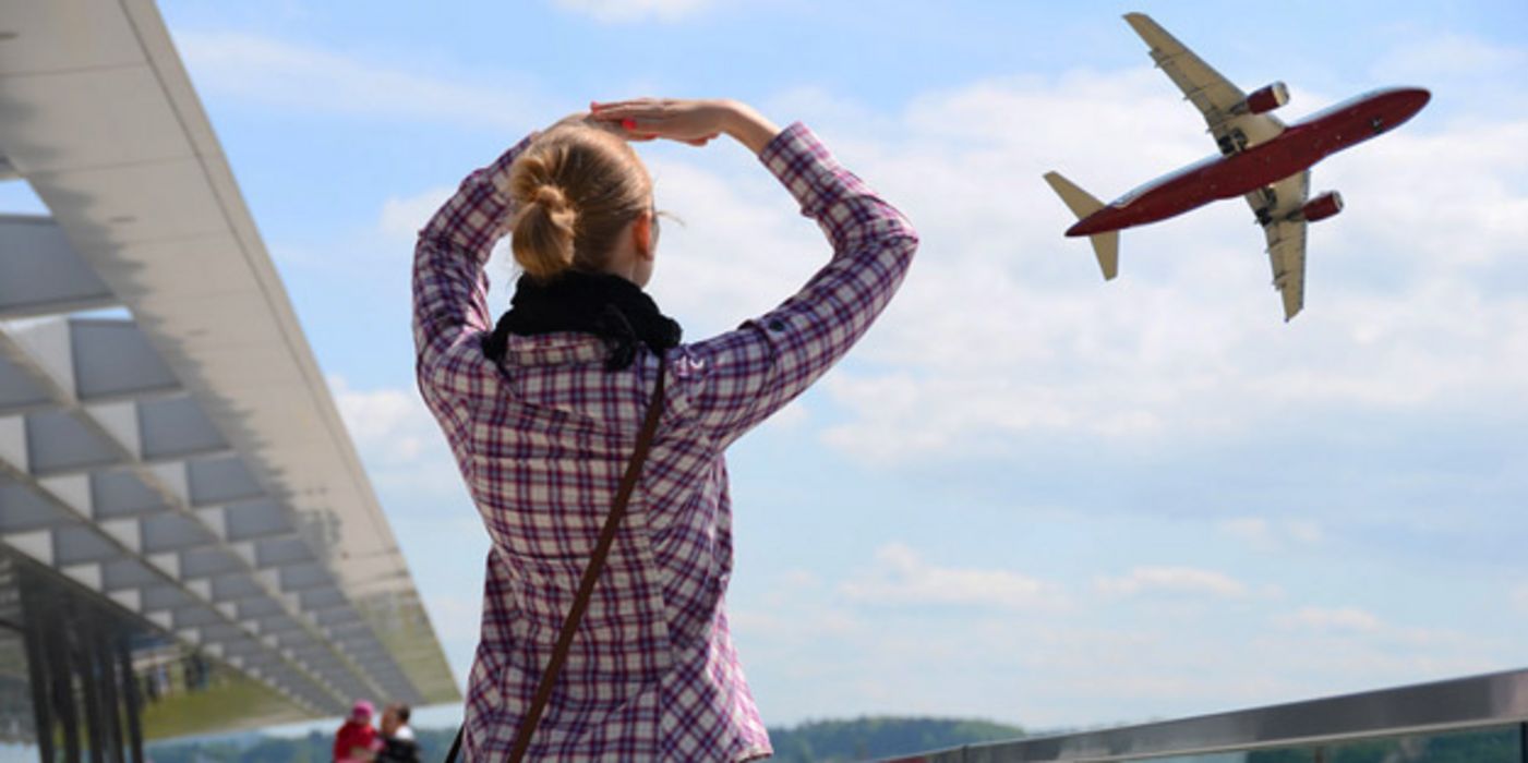 Szene vor Flughafen, Frau von hinten, Karohemd, Jeans, beobachtet Flugzeug beim Abflug