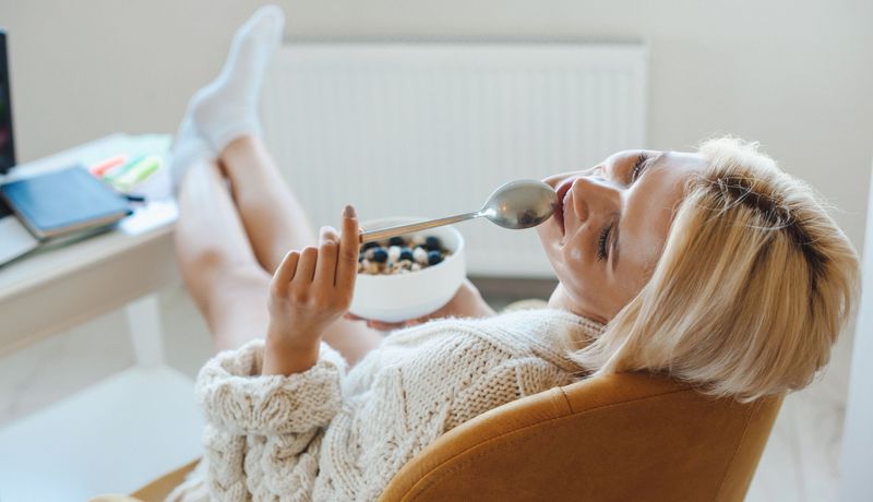 Junge Frau sitzt auch Sessel und hält einen Löffel und ein Müsli in den Händen.