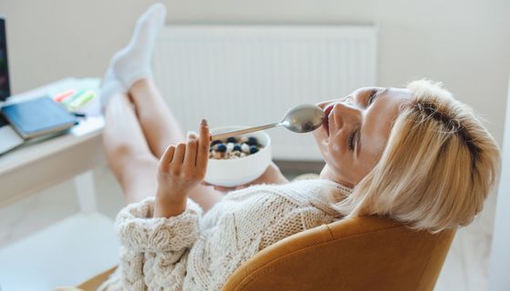 Junge Frau sitzt auch Sessel und hält einen Löffel und ein Müsli in den Händen.