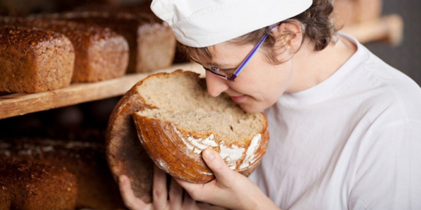 Jüngerer Bäcker hat ein Brot auseinandergebrochen und riecht genüsslich am Teig 