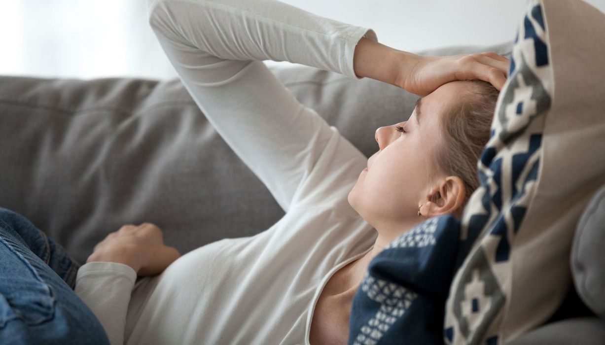 Junge Frau, liegt auf der Couch, erschöpft.