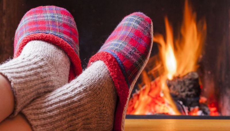 Zwei vor dem Kamin ausgestreckte Beine, die Füße stecken in Wollsocken und Pantoffeln